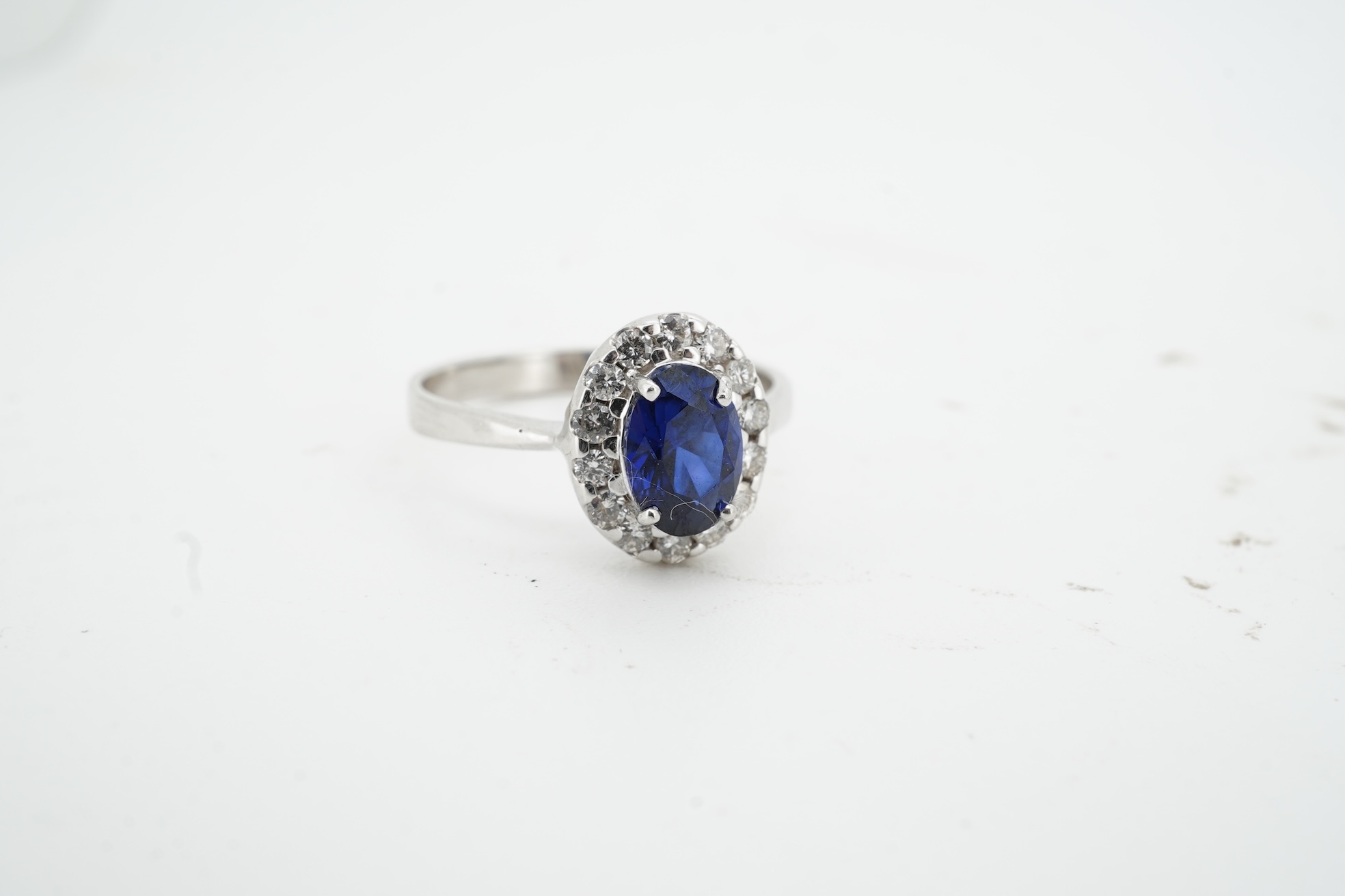 A synthetic sapphire and diamond cluster ring, mounted in white gold, size L1/2, stamped 18K, gross weight approximately 1.5 grams